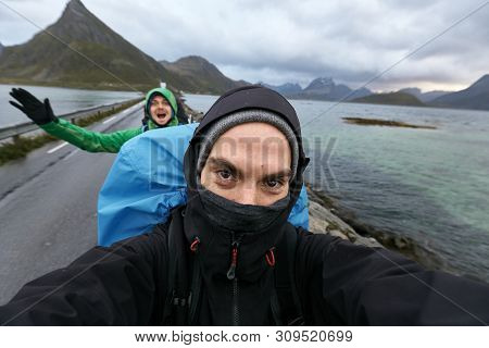 Self Portrait Of Two Young Men Hiking Behind Each Other On A Street On Lofoten Islands In Norway. Th