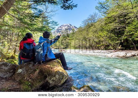 Man And Woman Sit On Rock Near Azusa River At Kamikochi In Northern Japan Alps.