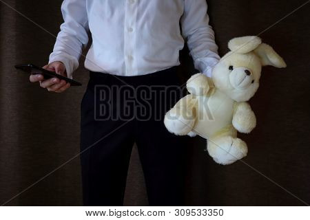 Young Man In A White Shirt And Black Pants Holding A Toy Hare And Phone. A Man With A Big Toy Rabbit