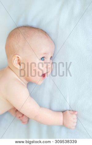 Profile Portrait Of Cute Little Baby Boy Lying On Blue Blanket And Looking Aside. Child With Open Mo