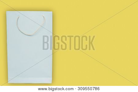 Light Blue Color Shopping Paper Bag On Yellow Background With Copy Space.