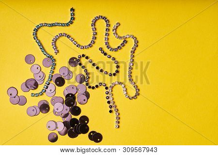 Embroidery Products And Tools. Black Sequins And Rhinestones On Yellow Background.