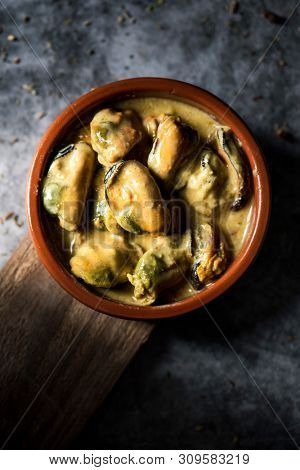 high angle view of an earthenware plate with mejillones al curry, spanish curried mussels, on a stone surface