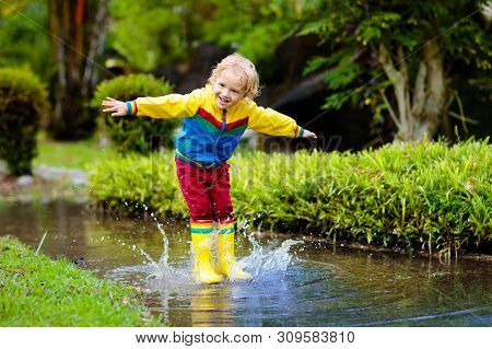 Child Playing In Puddle. Kids Jump In Autumn Rain