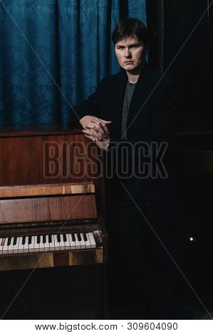 Classical Musician Performer Near Piano. Musical Artist In Dark Room Of Culture House. Portrait Of C