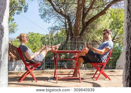 Couple On Vacations Resting In Front Of Bungalow House At Camping Site In Pure Nature. Family Vacati