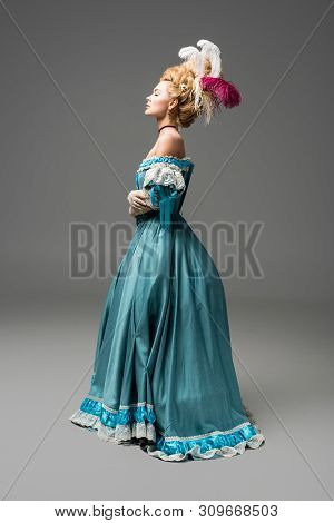 Side View Of Pompous Victorian Woman In Wig Standing In Blue Dress On Grey