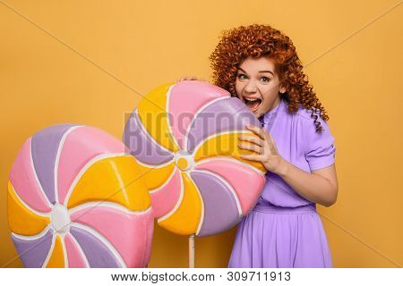 Mmm Yummy It Is Very Sweet Lollipop. Emotional Curly Haired Woman Bite Off Piece Candy On Yellow