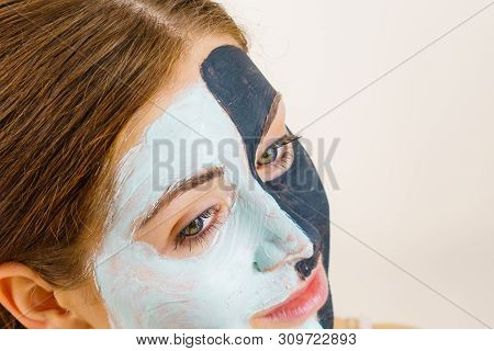 Woman With Clay Carbo Black Mask On Half Face And White Mud On Second Half. Girl Taking Care Of Oily
