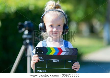 Portrait Of A Child With A Tv Clapper. Television Numerator. A Little Girl In Headphones With A Tv N