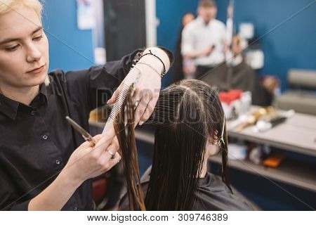 Hairdresser Holding Scissors And Comb And Makes Haircut Woman Client. Young Beautiful Woman Hair Cut