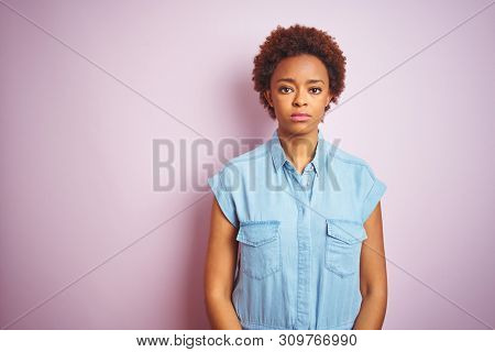 Young beautiful african american woman with afro hair over isolated pink background with serious expression on face. Simple and natural looking at the camera.
