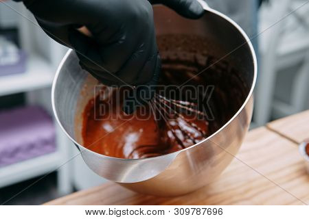Cooking Chocolate In A Water Bath. Hands Black Gloves Are Black. Chocolate In An Iron Pan.