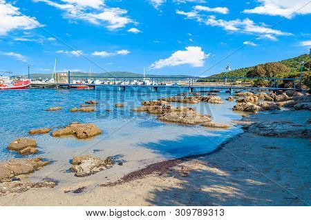 View Of Gulf, Pier And Beach Of Tramariglio In A Sunny And Cloudy Day, In The Capocaccia Coast