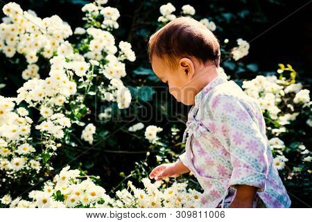 Baby boy wearing traditional Nepali daura bhoto plays with white flowers in garden