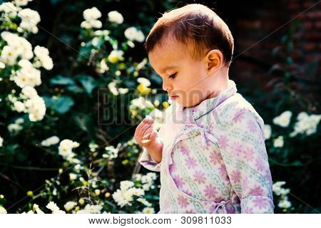 Baby boy wearing traditional Nepali daura bhoto plays with white flowers in garden
