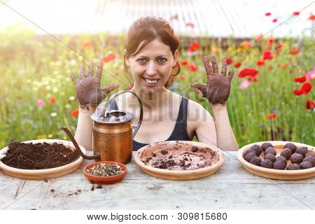 Woman Is Manufacturing Seed Balls Or Seed Bombs On A Wooden Table, Flower Field In The Background