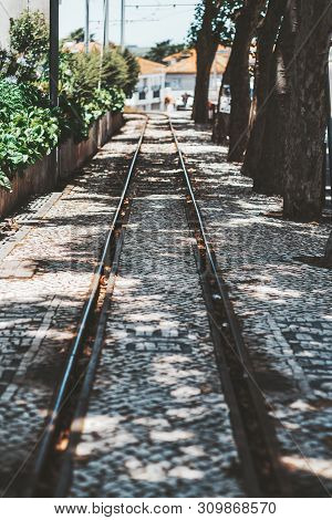 A Narrow Tramway Track For A Traditional Tram Surrounded By Trees And A Stone Fence, With A Paving S