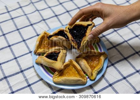 Woman Hand Holding Hamantash Purim Blueberry And Apricot Jam Cookies On Colored Plate On Blue And Wh