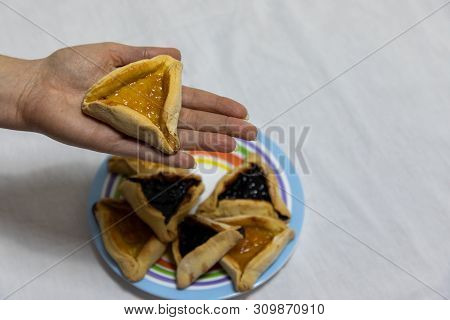 Woman Hand Holding Hamantash Cookie On Top Of Colorful Plate With More Hamantash Cookies