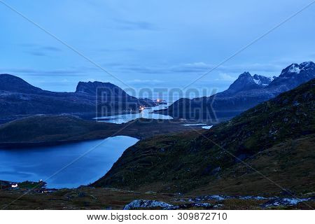 View from above over a bay with snowcapped mountains during evening blue hour on Lofoten Islands in