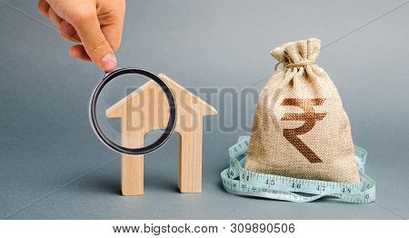 Bag With Money And Tape Measure With A Wooden Houses. The Concept Of A Limited Real Estate Budget. M