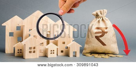 Money Bag With A Sign Indian Rupee (rupiah) And Down Arrow With Wooden Houses. The Concept Of Fallin