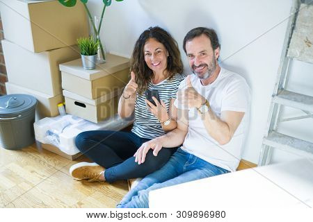 Middle age senior couple moving to a new home using smartphone happy with big smile doing ok sign, thumb up with fingers, excellent sign
