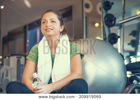 Woman, A Break In The Gym, Sitting On A Pilates And Fitness Ball With A Towel Around Her Neck And Wi