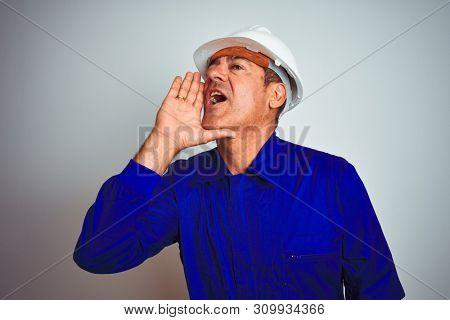 Handsome middle age worker man wearing uniform and helmet over isolated white background shouting and screaming loud to side with hand on mouth. Communication concept.