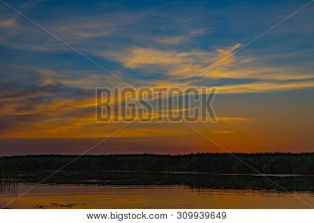 Picturesque Summer Sunset Over The Lake, Overgrown With Reeds. Pink And Gold Clouds Are Reflected In