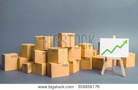 A Large Number Of Cardboard Boxes And Sign With Green Up Arrow. Rate Growth Of Production Of Goods A