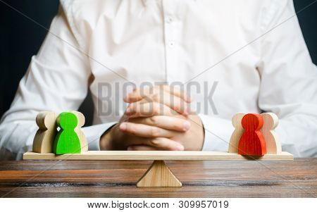 A Man With Hands In The Gesture Of A Lock And Looks At The Red And Green Standoff Groups On A Scales