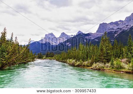 Bow River In Canmore With The Canadian Rockies Mountain Ranges Of The Three Sisters And Ehagay Nakod
