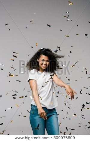 Happy African American Woman Smiling And Gesturing Near Falling Confetti While Standing On Grey