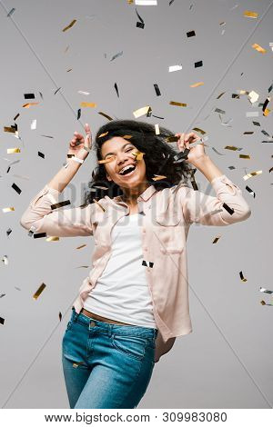 Positive Young African American Woman Smiling Near Shiny Confetti While Standing On Grey
