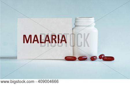 On A Light Blue Background A Card With The Text Malaria Near The White Bottle Pills.
