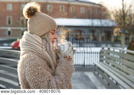 Woman Wear White Mittens Holding Steaming White Cup Of Hot Coffee Or Tea In Cold Winter Sunny Day, S