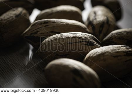 A Macro Shot With Selective Focus Of A Handful Of Pecan Nuts In Shells Set On A Wood Table.