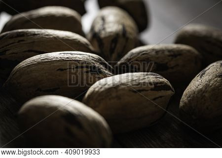 A Macro Shot With Selective Focus Of A Handful Of Pecan Nuts In Shells Set On A Wood Table.