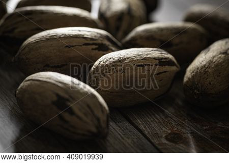 A Macro Shot With Selective Focus Of A Handful Of Pecan Nuts In Shells Set On A Wood Table.