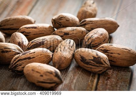 A Macro Shot With Selective Focus Of A Handful Of Pecan Nuts In Shells Set On A Wood Table.