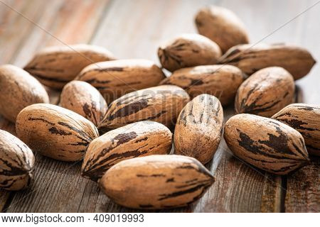 A Macro Shot With Selective Focus Of A Handful Of Pecan Nuts In Shells Set On A Wood Table.