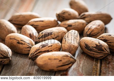 A Macro Shot With Selective Focus Of A Handful Of Pecan Nuts In Shells Set On A Wood Table.