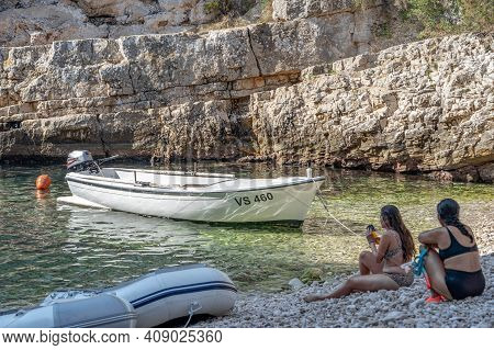 Vis, Croatia - Aug 17, 2020: Females Sit On Sheltered Cove Stiniva Beach In Summer