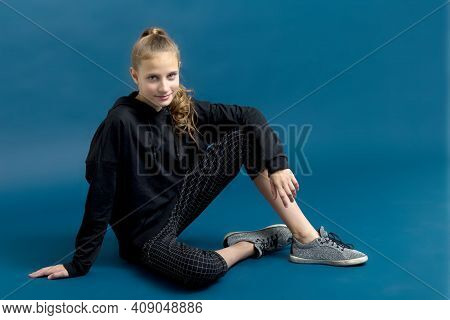 Teen Girl In Black Hoodie Sitting On Floor. Portrait Of Beautiful Serious Teenager Dressed Black Swe
