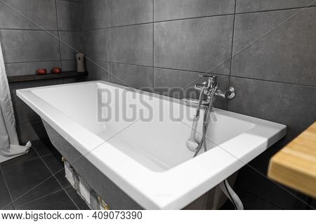 Bathroom Interior With Grey Tile On A Wall, Stylish White Bath With A Silver Tap. Minimalism In Inte