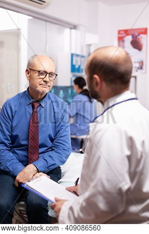 Senior Man Receive Healthcare Treatment From Doctor In Hospital Examination Room. Elderly Patient Ha