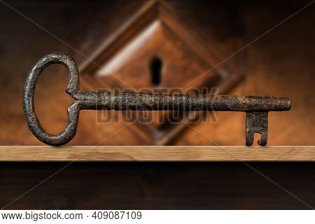 Extreme Closeup Of An Old And Vintage Rusty Key On A Wooden Shelf With A Wood Keyhole On Background.