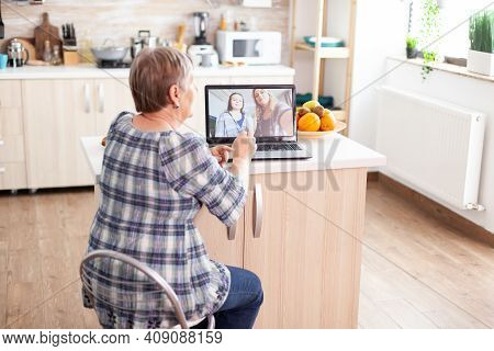 Happy Senior Woman During A Video Conference With Family Using Laptop In Kitchen. Online Call With D